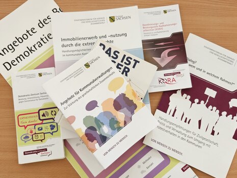 Stapel mit Informationsbroschüren zu Demokratie und Extremismusprävention, herausgegeben vom Sächsischen Sozialministerium.