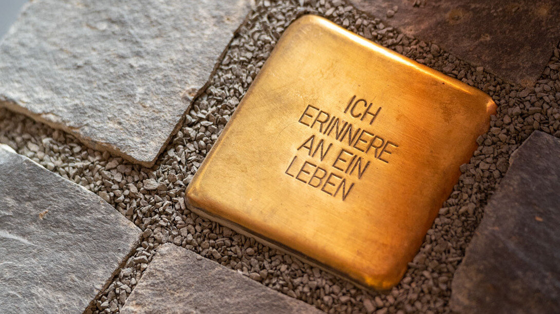 Auf dem Bild ein Stolperstein . eingelassen in einen Weg aus Kopfsteinpflaster. Auf dem Stolperstein steht: Ich erinnere an ein Leben.