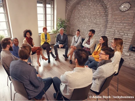 Diverse Gruppe im Stuhlkreis bei Gesprächsrunde in modernem Raum mit Backsteinwand und Holzboden.
