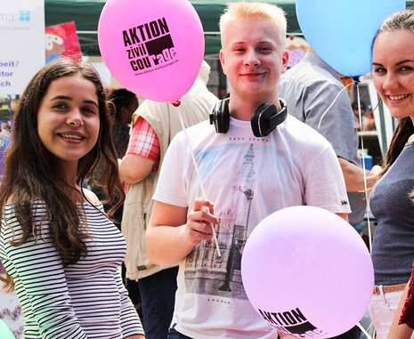Das Bild zeigt mehrere junge Menschen auf einer Freiluftveranstaltung. Sie stehen eng beieinander und halten farbige Luftballons mit dem Aufdruck Aktion Zivilcourage in den Händen. Einer der Jugendlichen trägt ein T-Shirt mit einem Motiv von London und Ko
