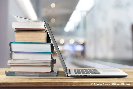 Bücherstapel und Laptop auf Schreibtisch symbolisieren Wissen, Bildung und digitales Lernen.