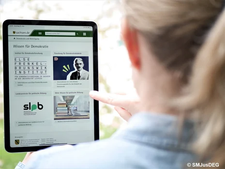 Person betrachtet Tablet mit Website „Wissen für Demokratie" zu Bildungsangeboten und politischer Bildung in Sachsen.