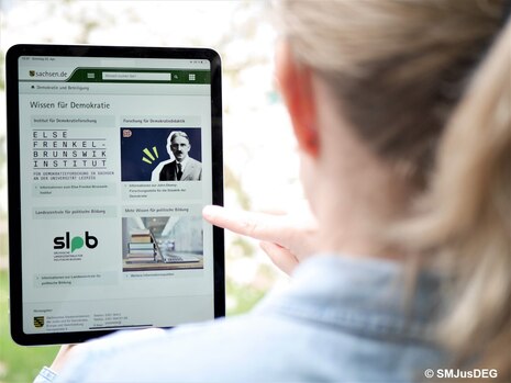 Person betrachtet Tablet mit Website „Wissen für Demokratie" zu Bildungsangeboten und politischer Bildung in Sachsen.