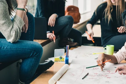 Gruppe bei Workshop-Arbeit. Menschen sitzen im Kreis, arbeiten gemeinsam an Papieren und Skizzen auf dem Boden.